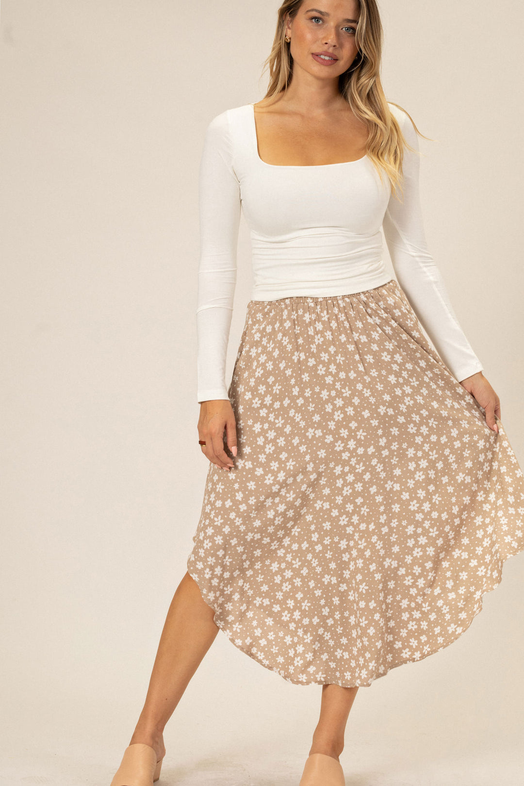 A white long-sleeved top paired with a tan and white floral print midi skirt, featuring a rounded hem and a flowy silhouette.