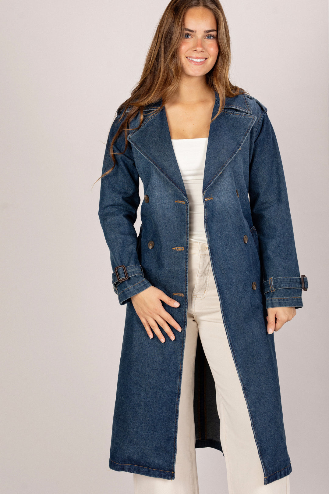 Woman wearing a long denim coat on a plain background