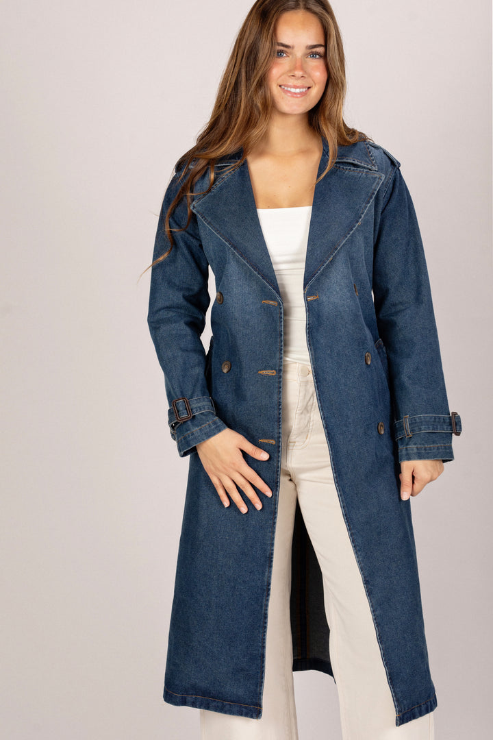 Woman wearing a long denim coat on a plain background
