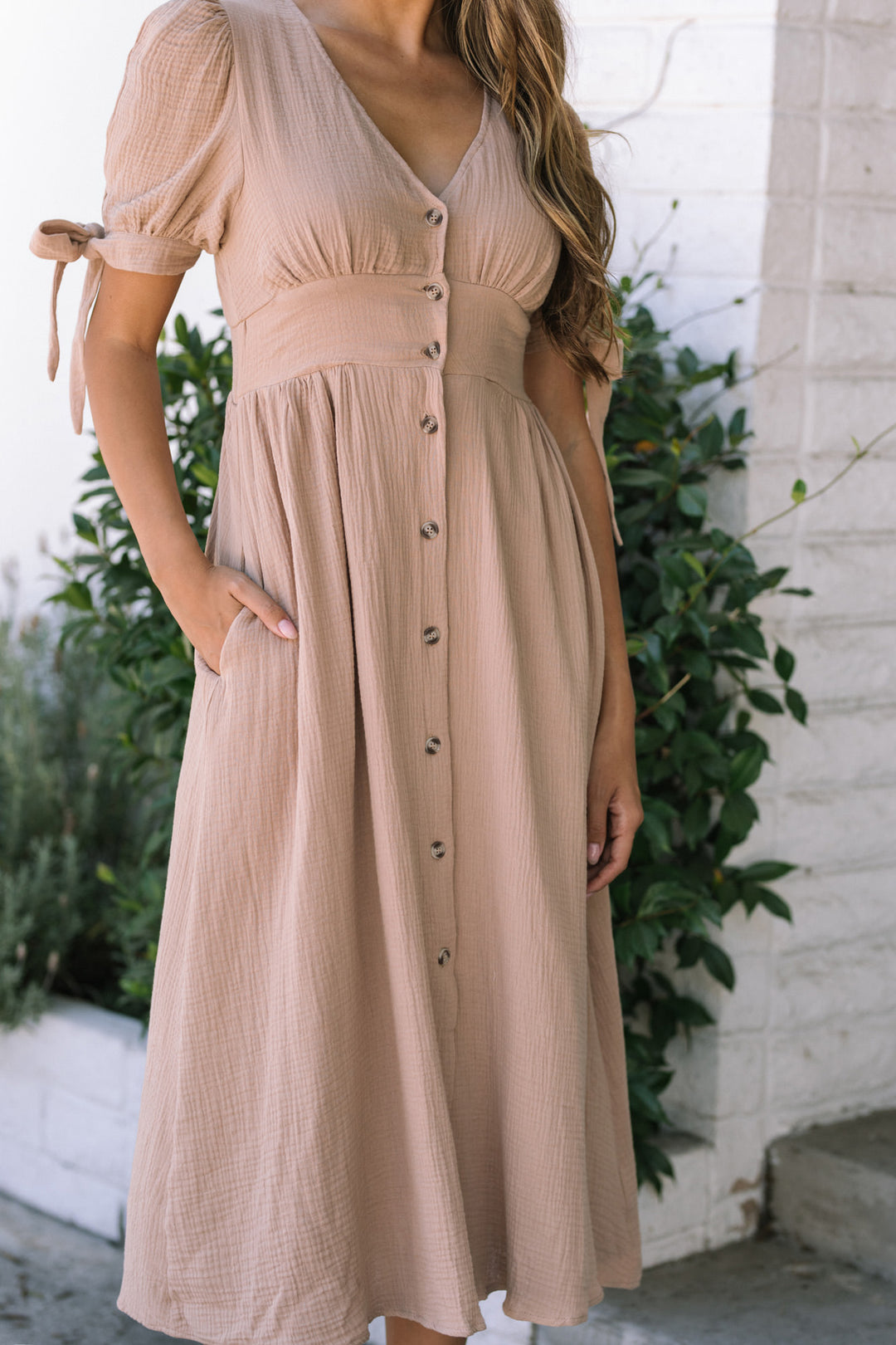 A tan, midi-length dress with a v-neck, puffy short sleeves, and button-down front, featuring a cinched waist and flowing skirt.