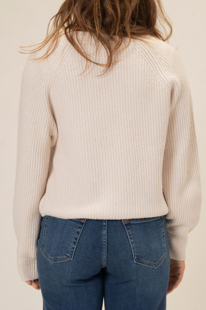 Ribbed beige knit cardigan with buttons, worn over light wash denim jeans.