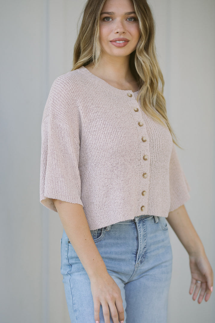 A pale pink, ribbed knit cardigan with short sleeves and button-front closure, featuring a relaxed, casual style.