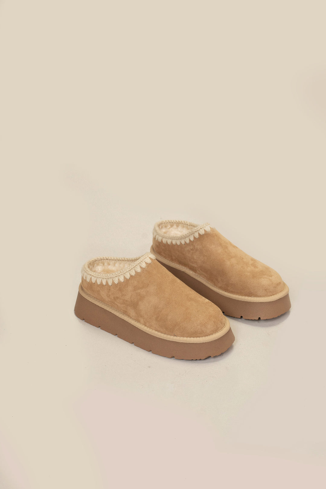 Tan suede platform mules with contrasting white stitching, designed for cozy comfort.
