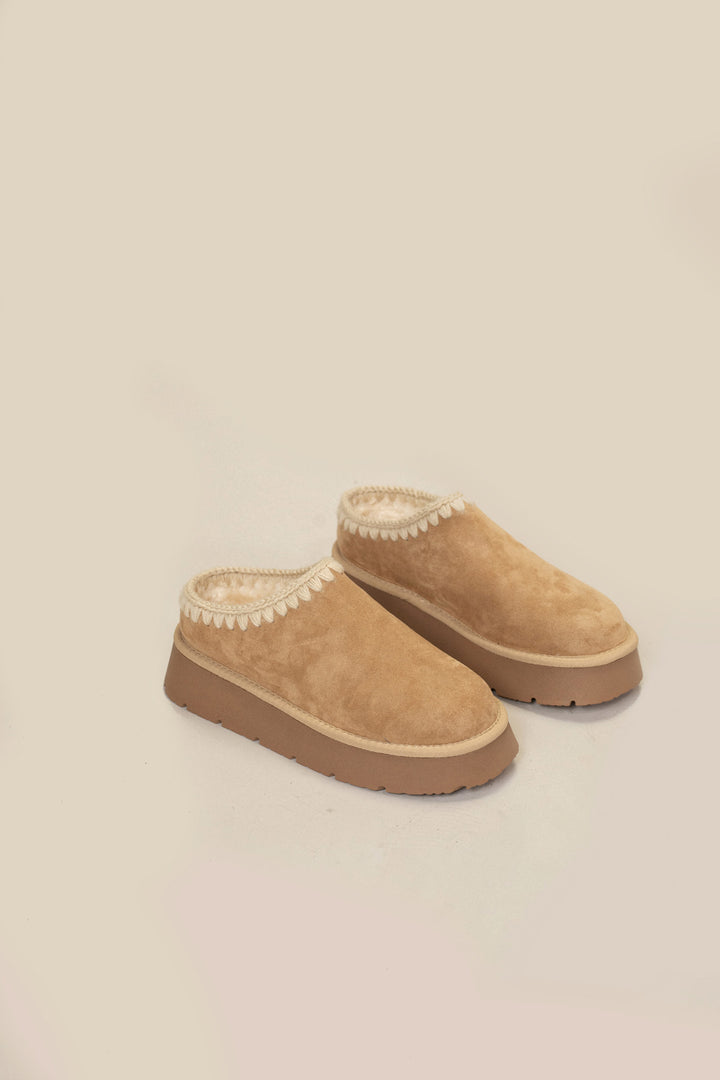 Tan suede platform mules with contrasting white stitching, designed for cozy comfort.
