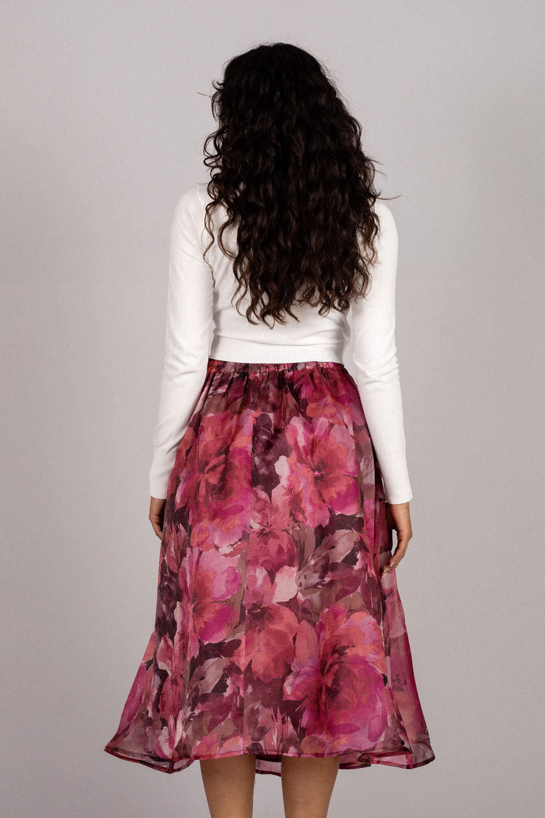 A floral midi skirt with a vibrant pink and burgundy floral print, worn by a model with long dark curly hair.