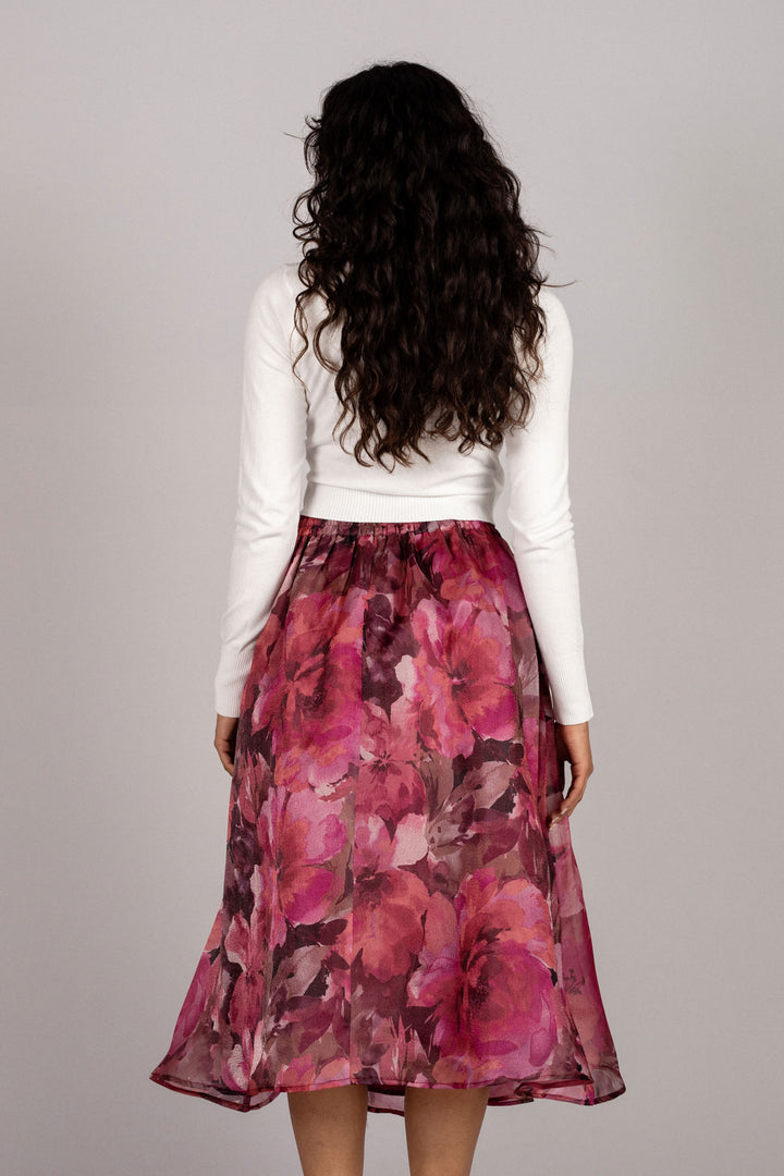 A floral midi skirt with a vibrant pink and burgundy floral print, worn by a model with long dark curly hair.