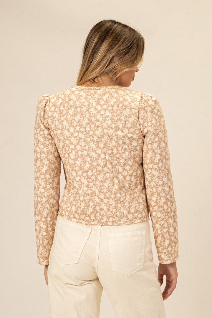 A floral-patterned, cream-colored jacket with puff sleeves, a button front, and a tie waist detail.