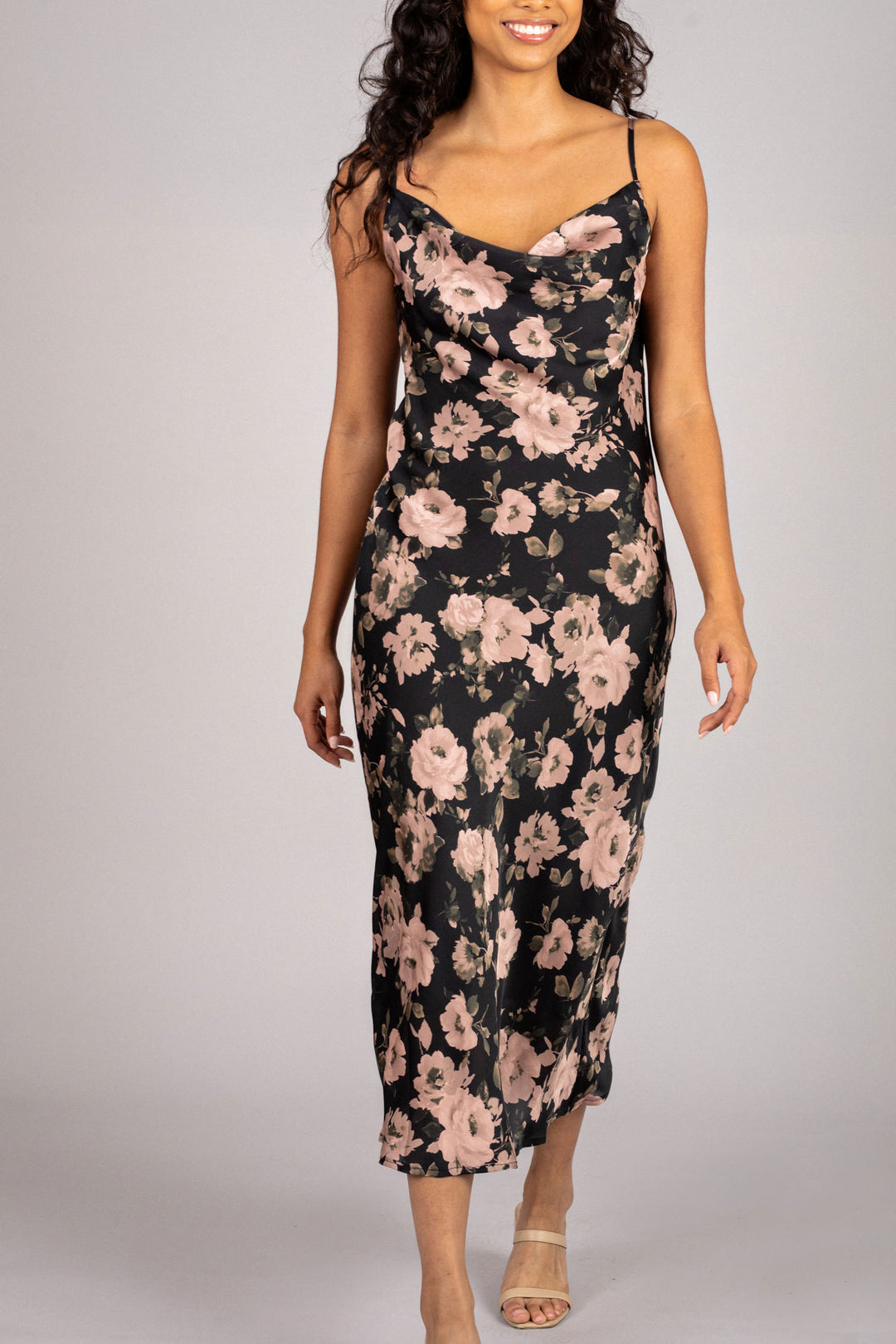 A sleeveless dress with a cowl neckline, featuring a vibrant floral print in shades of pink and black against a dark background. The dress has a fitted silhouette and a midi length.