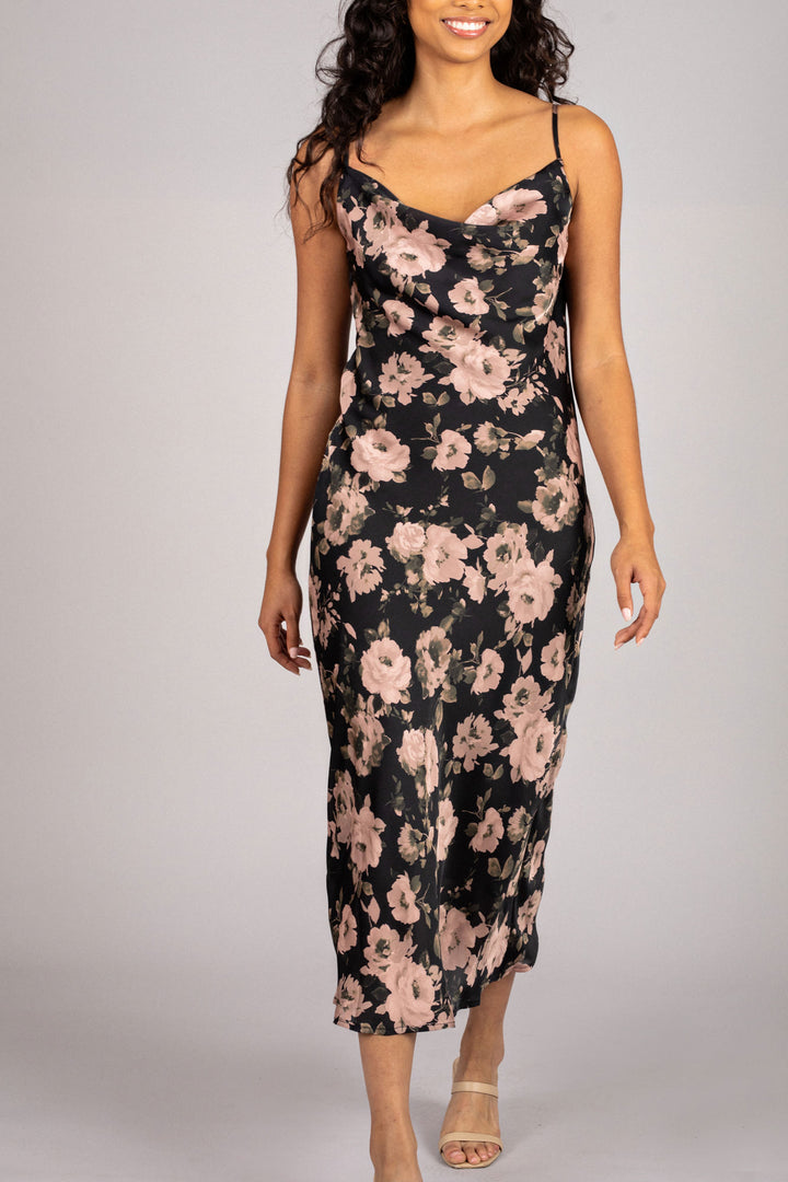 A sleeveless dress with a cowl neckline, featuring a vibrant floral print in shades of pink and black against a dark background. The dress has a fitted silhouette and a midi length.