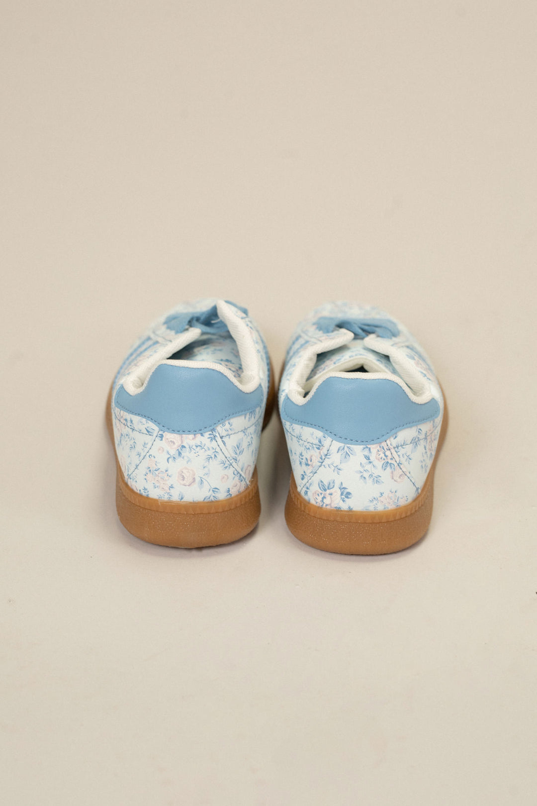 Pair of light blue floral print sneakers with lace-up closure and gum sole, showcasing a stylish and feminine design.