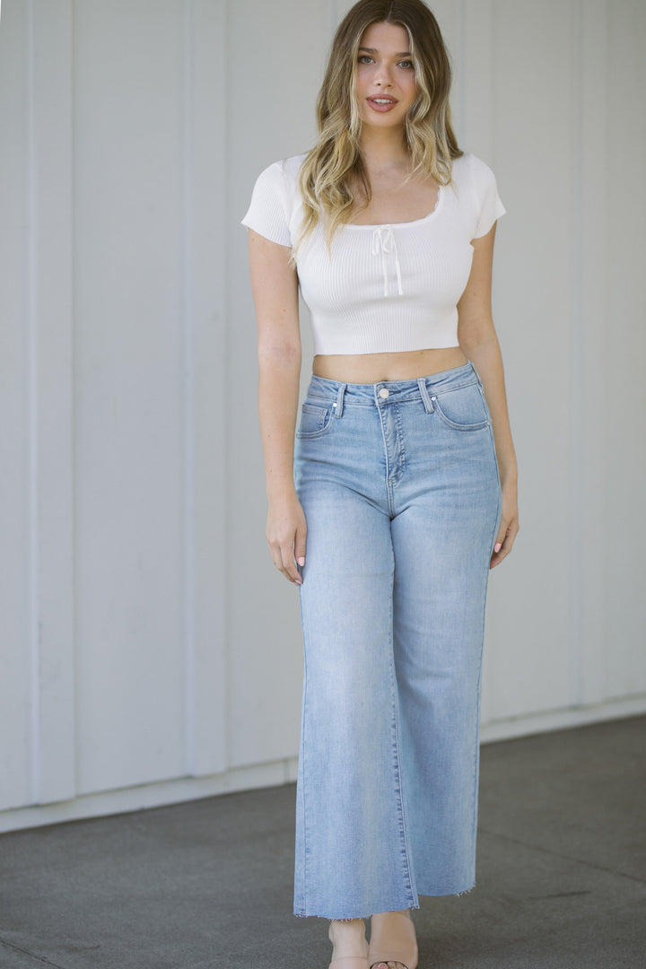 Cropped wide-leg light wash denim jeans with high-waist design and frayed hems, worn with a white fitted ribbed crop top.