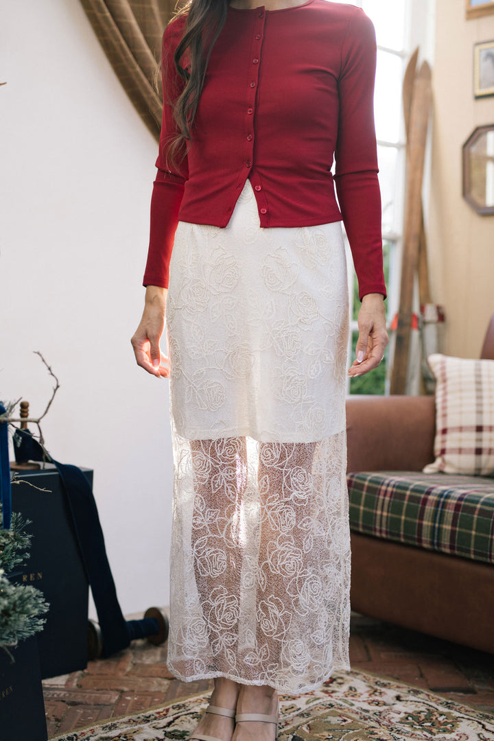 A burgundy ribbed knit top with a buttoned front, worn with a white lace midi skirt.