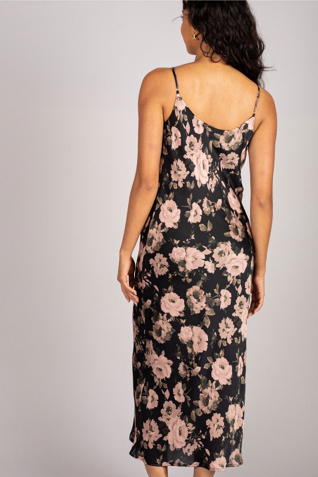 A flowy black slip dress with delicate pink floral print, featuring adjustable spaghetti straps and a midi length.