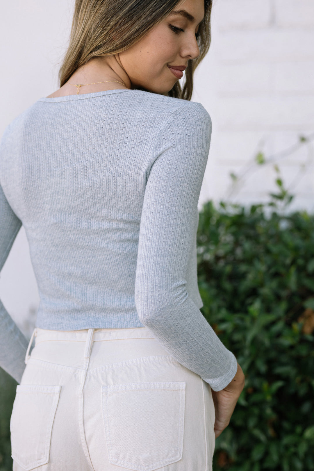 Soft gray ribbed knit top with long sleeves and a tie-front design, worn with high-waisted white pants.