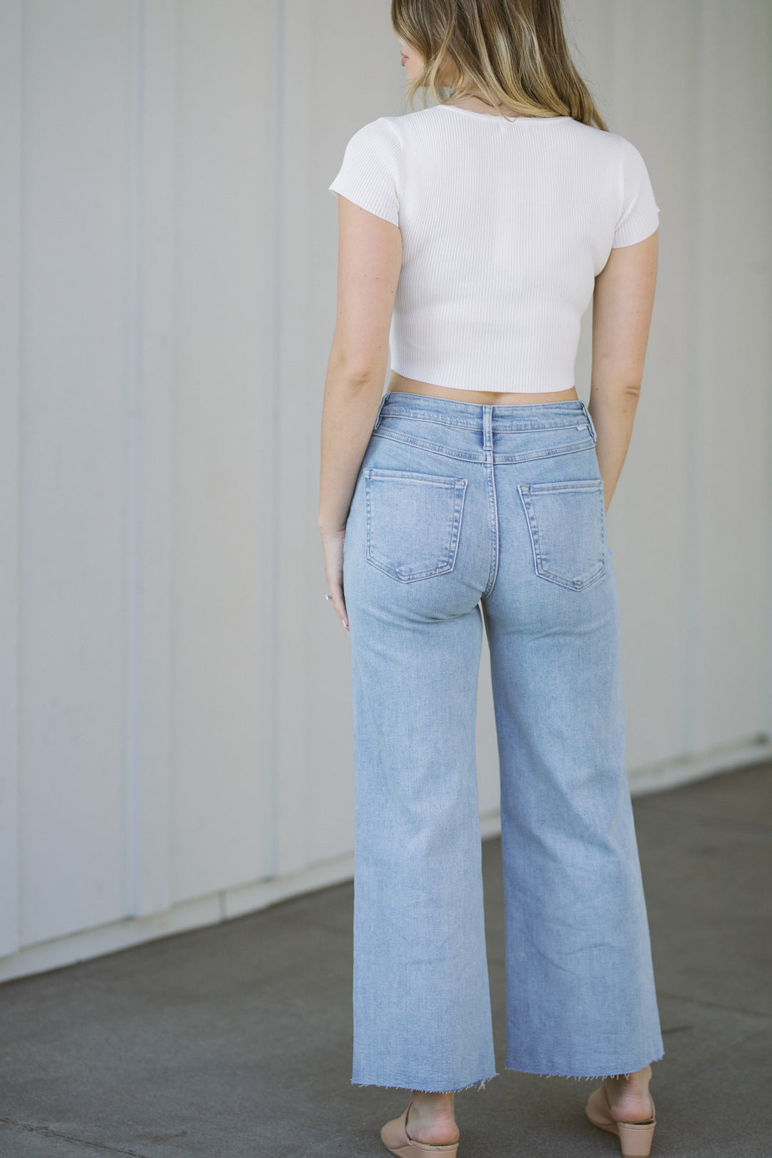 A close-up view of the back of a person wearing a white, ribbed-knit crop top with a high neckline and wide-leg light wash denim jeans.