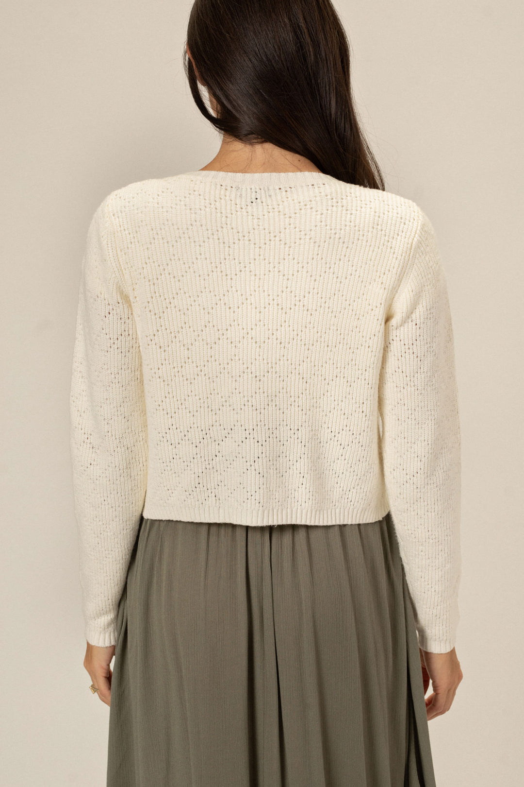 A close-up view of the back of a white knit cardigan with a textured diamond pattern, worn over a gray skirt.
