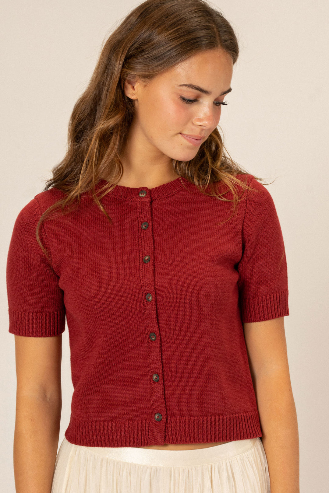 Red knit buttoned top with short sleeves and a ribbed texture, worn by a woman with long brown hair.