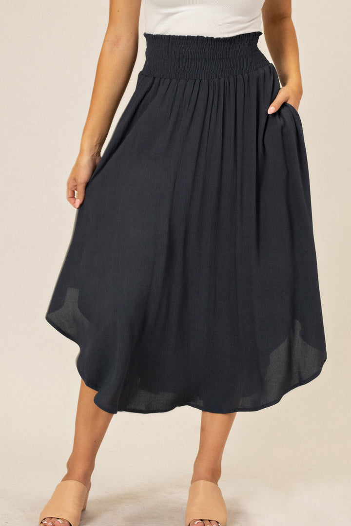 A flowing, navy blue midi skirt with a round hemline and a high, smocked waistband.
