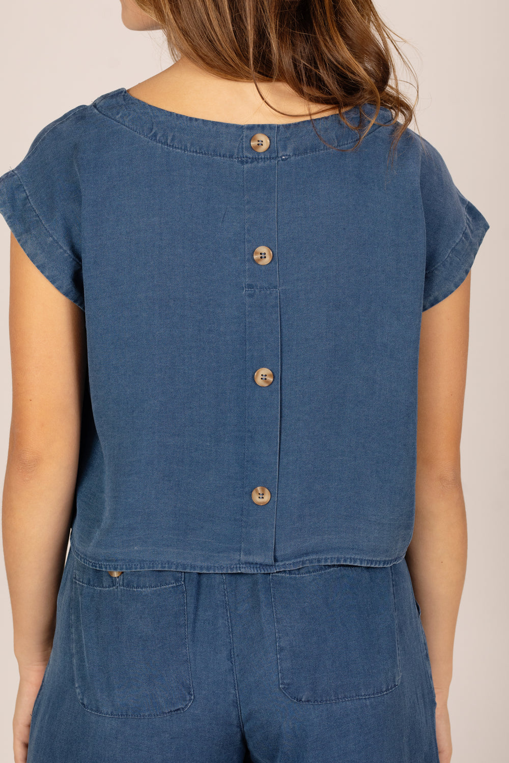 Blue denim jumpsuit with button details on a neutral background