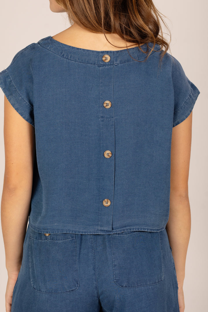 Blue denim jumpsuit with button details on a neutral background