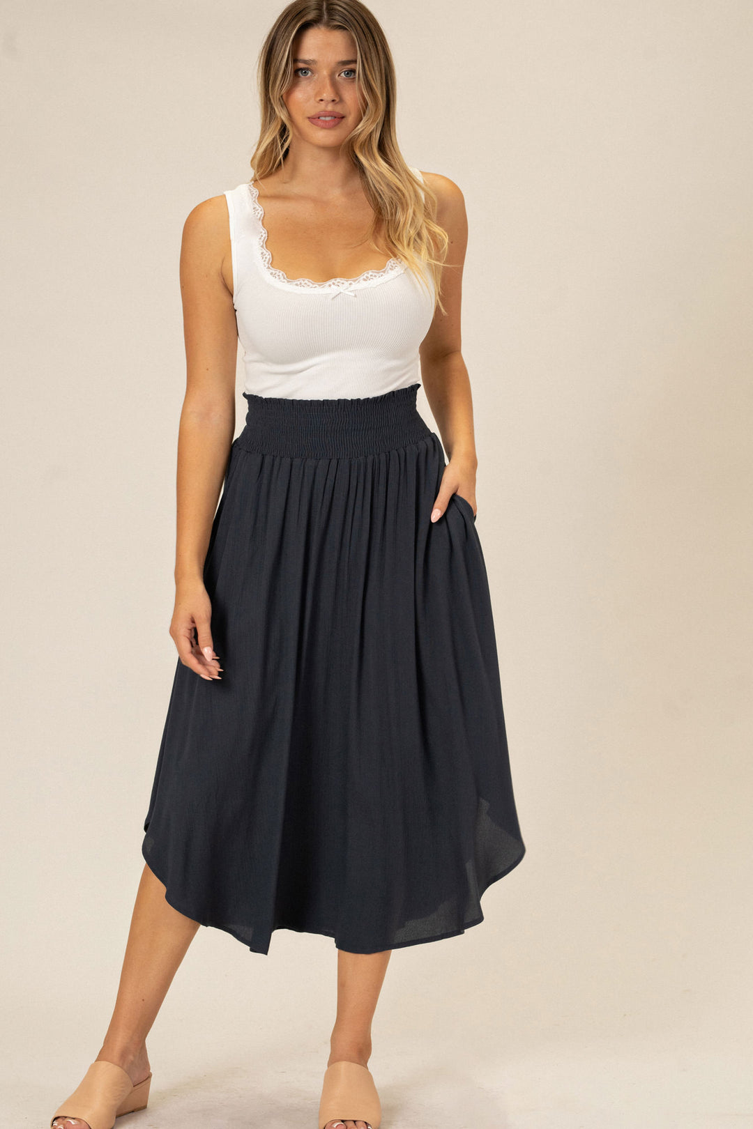 A white tank top with lace trim and a black midi skirt with a rounded hemline, worn by a woman with long blonde hair.