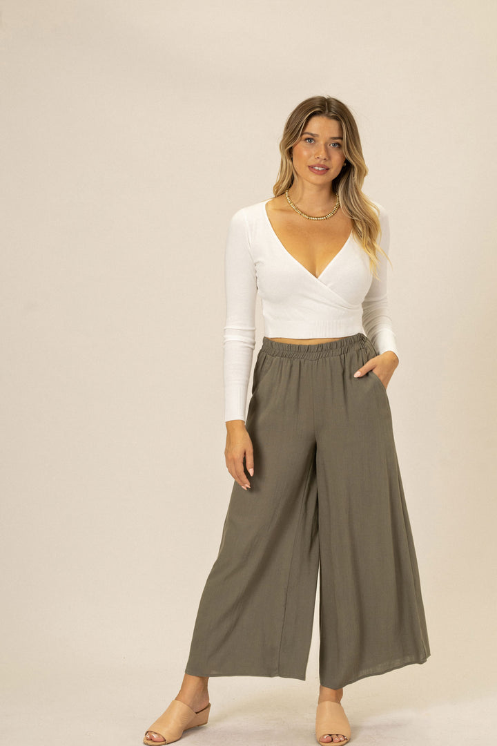A young woman in a white wrap-style top and gray wide-leg pants stands against a neutral background, showcasing the relaxed fit and versatile style of the Charlie Wide Leg Pants.