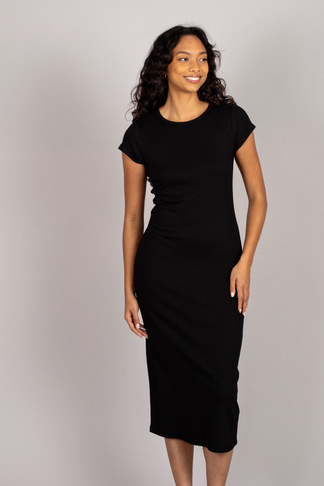 A woman wearing a black midi dress with short sleeves and a slim, figure-flattering silhouette, smiling confidently.