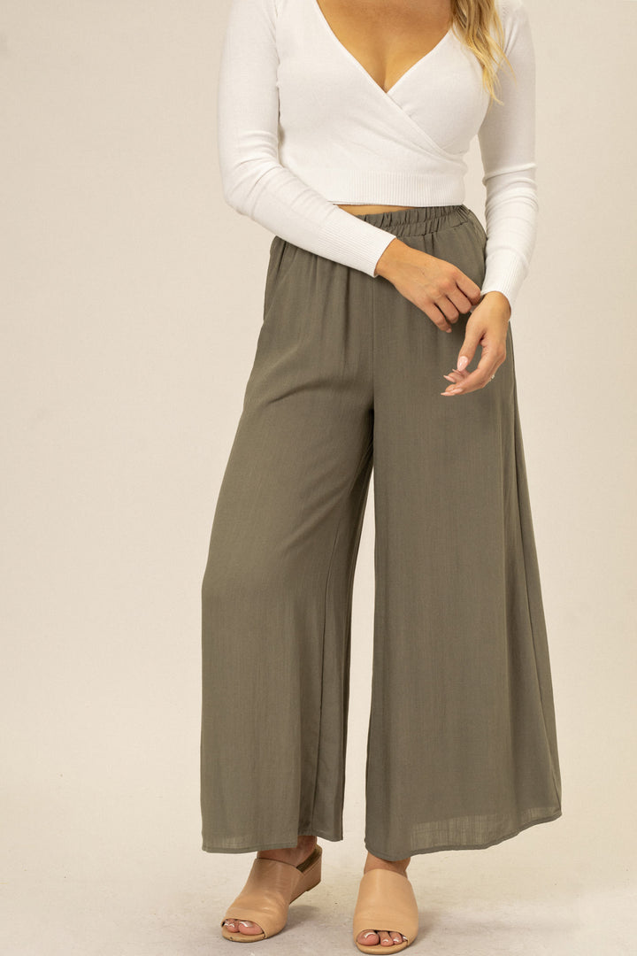 Olive-green wide-leg pants with elastic waistband, modeled by a person wearing a white cropped top and neutral sandals.