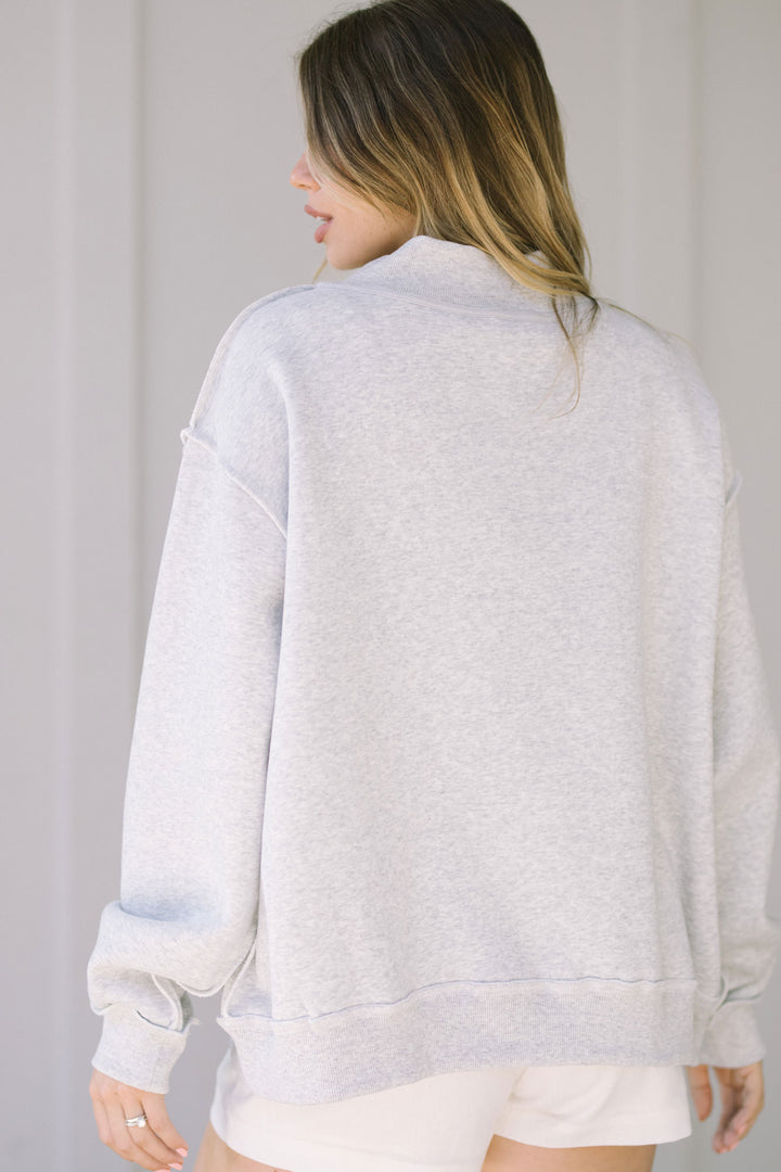 A gray, mock-neck sweatshirt with a loose, relaxed fit and long sleeves, styled with a side-zip detail for a unique look.