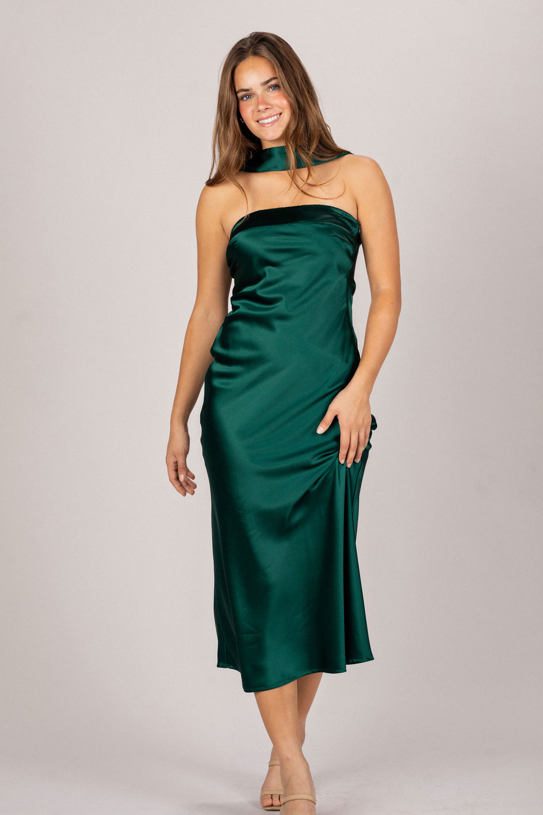 A green satin dress with a high neckline and a flowing, midi-length silhouette, worn by a smiling woman with long, dark hair.