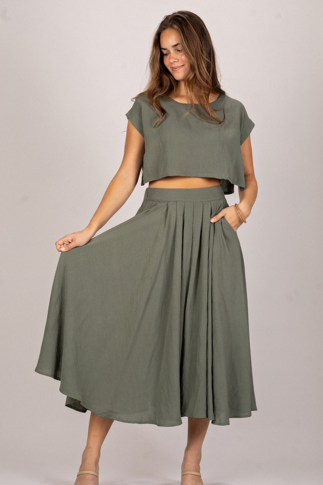 Woman wearing a green outfit with a top and skirt on a plain background