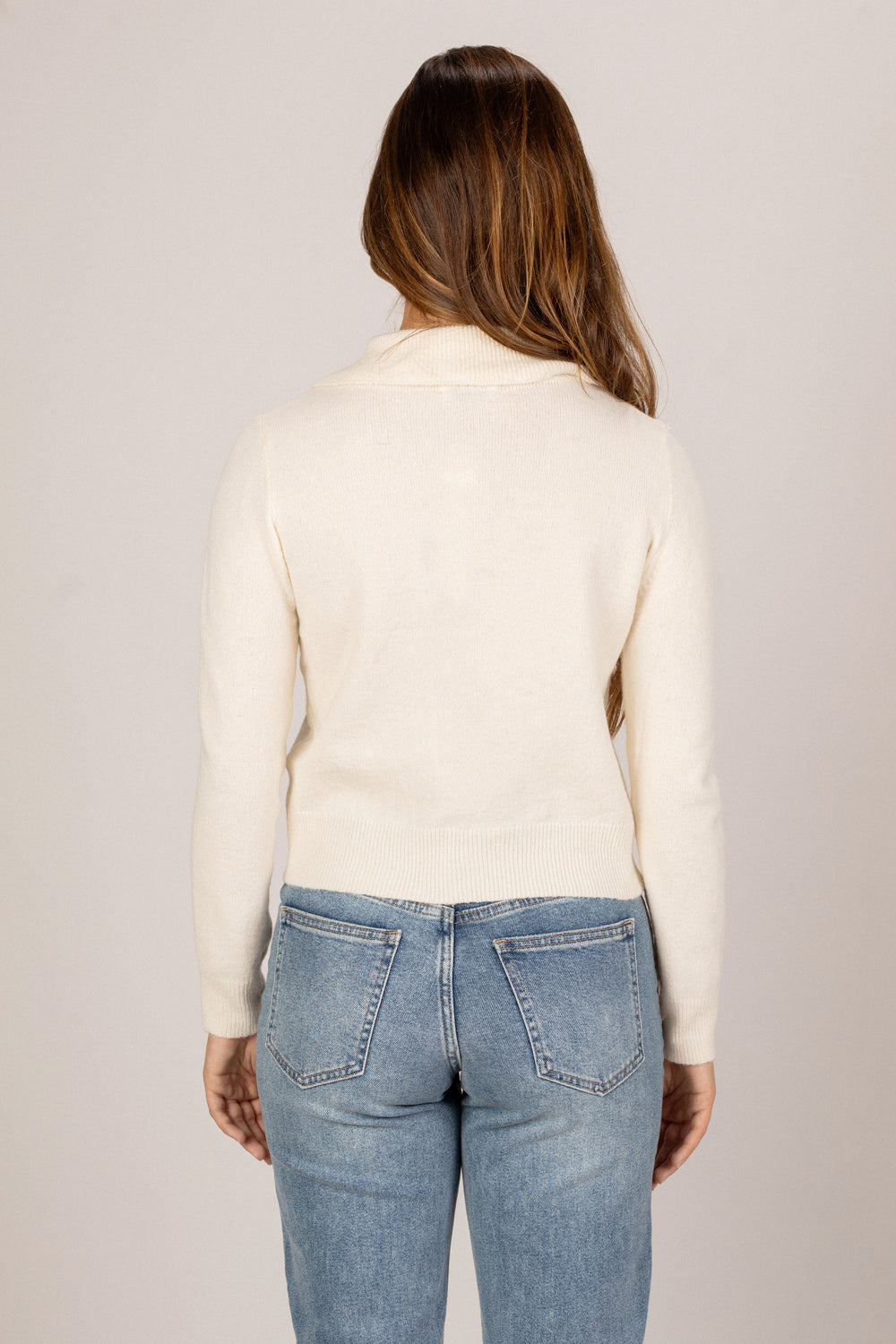 A cream-colored knit top with a collared neckline, featuring a slim fit and long sleeves. The model has long, dark brown hair and is wearing size Small.