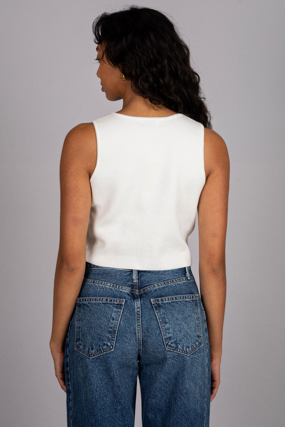 A sleeveless white vest top with a V-neckline, worn with high-waisted blue denim jeans.