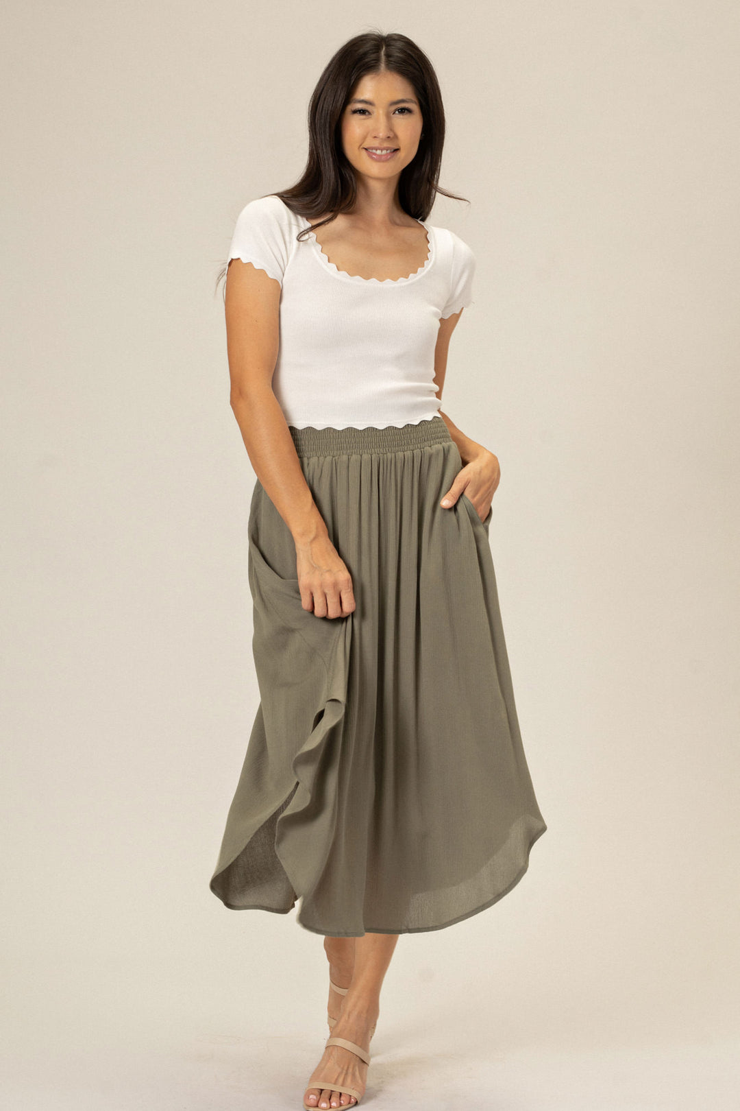 A woman wearing a gray pleated midi skirt with a comfortable elastic waistband, paired with a white scalloped tank top.