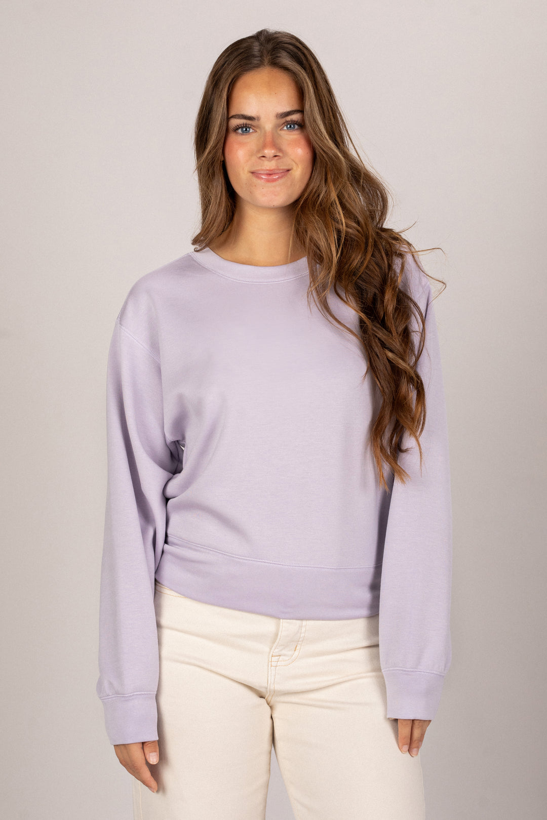 A young woman with long brown hair is wearing a relaxed, light purple sweatshirt with a simple round neckline.