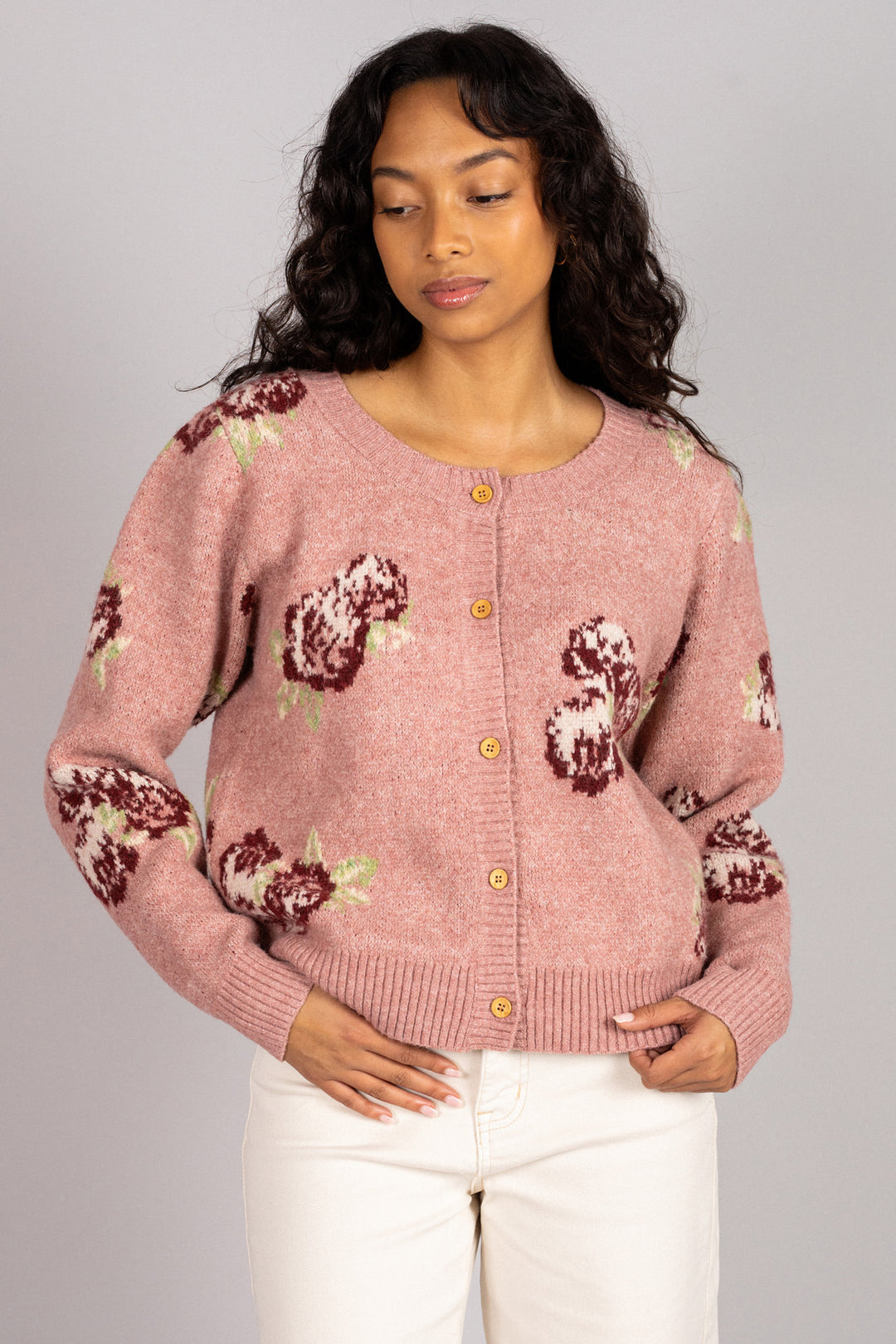 Woman wearing a pink knit cardigan with brown floral patterns, buttons down the front, and long sleeves.