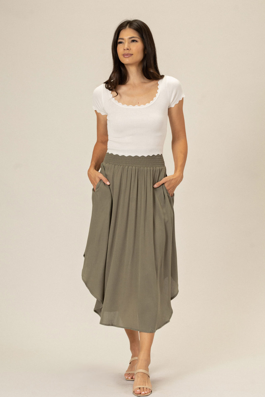 A woman wearing a white top and gray midi skirt with a scalloped waistband, pockets, and a relaxed, flowing silhouette.