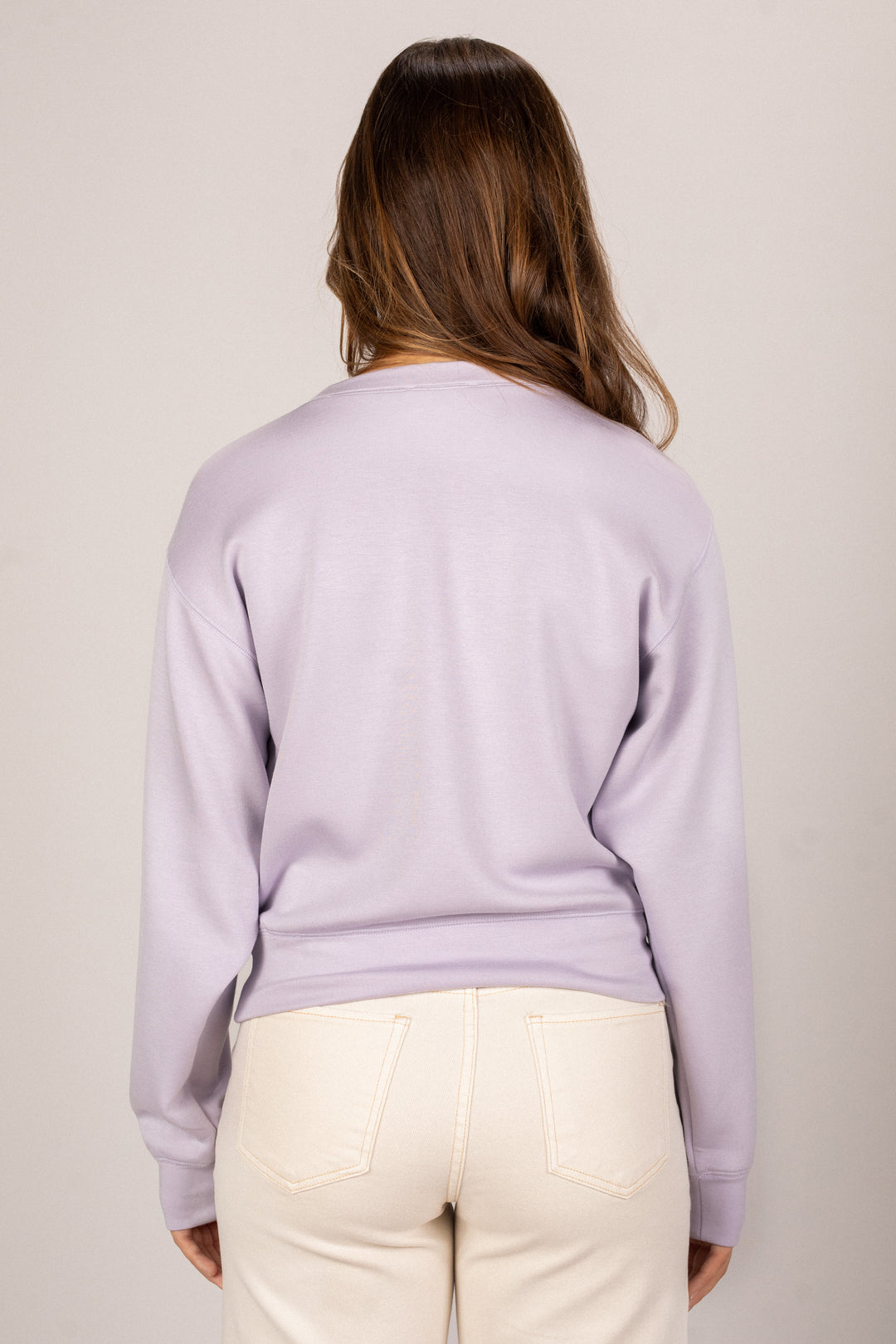 A woman wearing a relaxed, light lavender sweatshirt with a high collar, standing against a beige background.