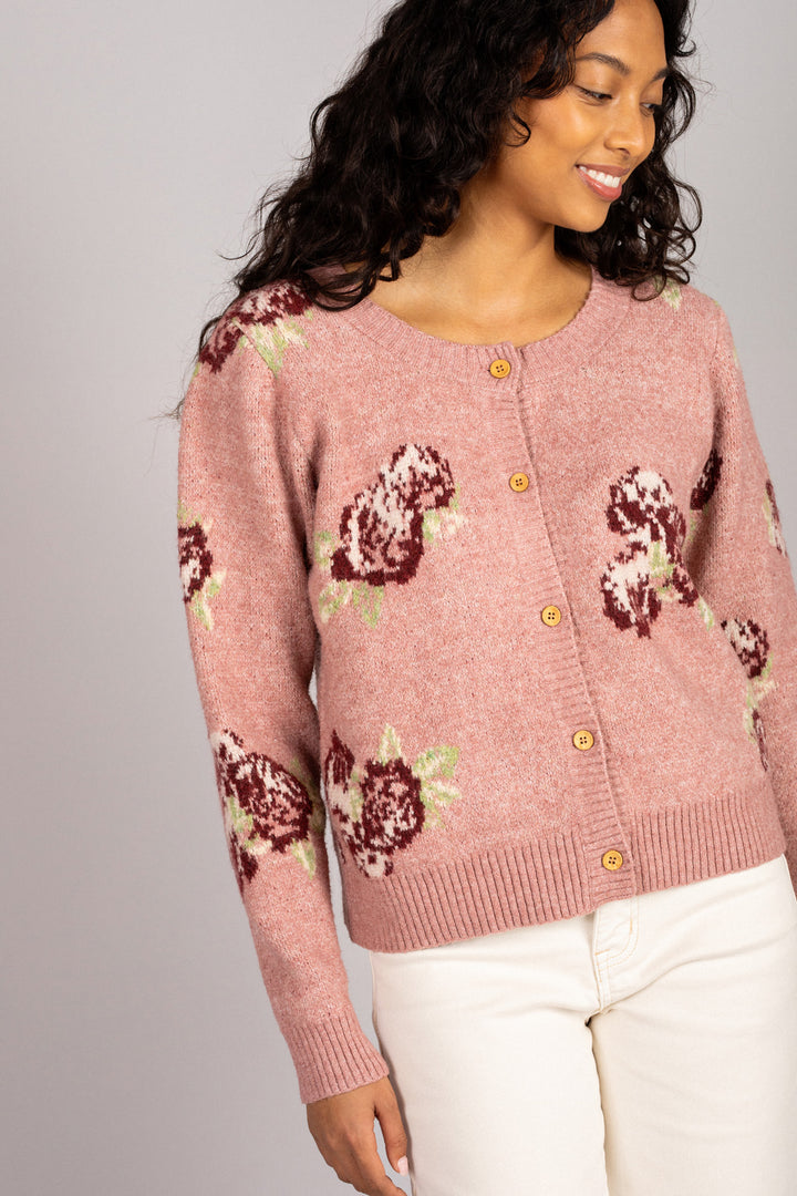 A pink, floral-patterned knit cardigan with button closure, worn by a smiling woman with curly black hair.
