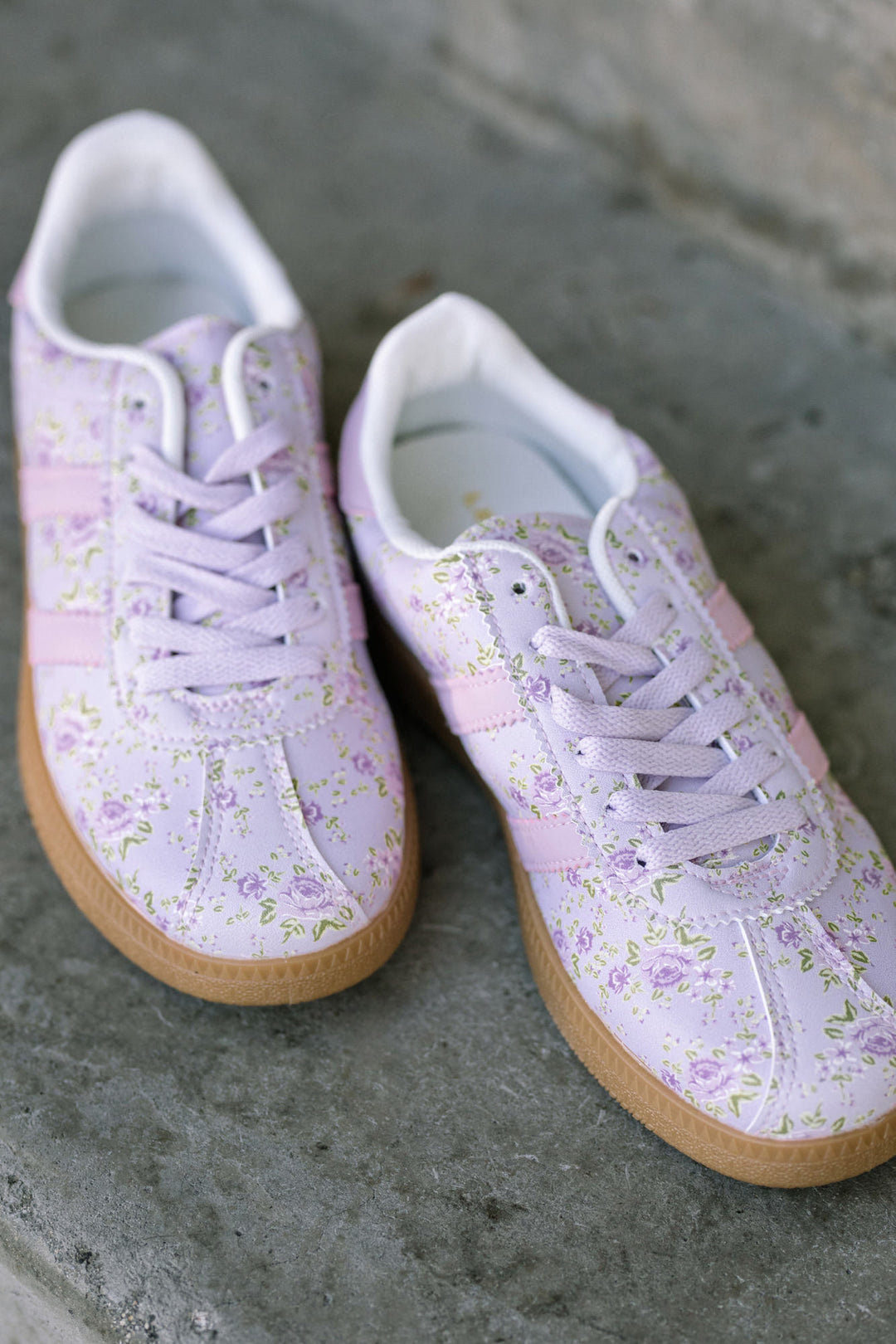 Two white sneakers with a delicate floral print pattern and gum rubber soles, tied with white laces.