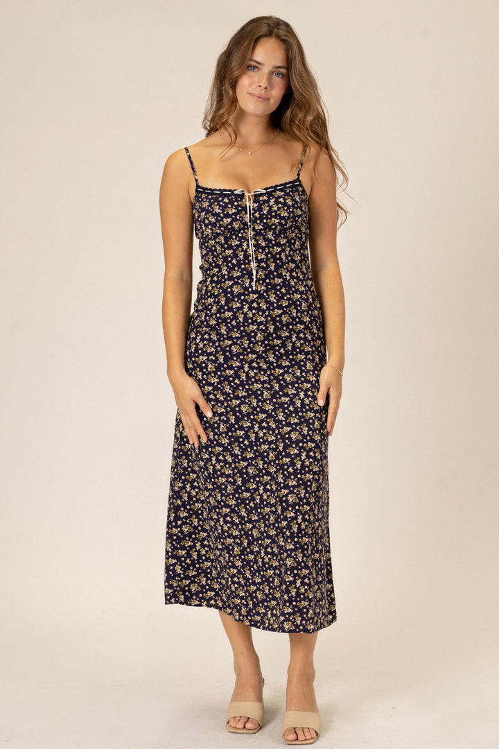 Woman wearing a navy blue floral print midi dress with spaghetti straps and a front zipper closure.