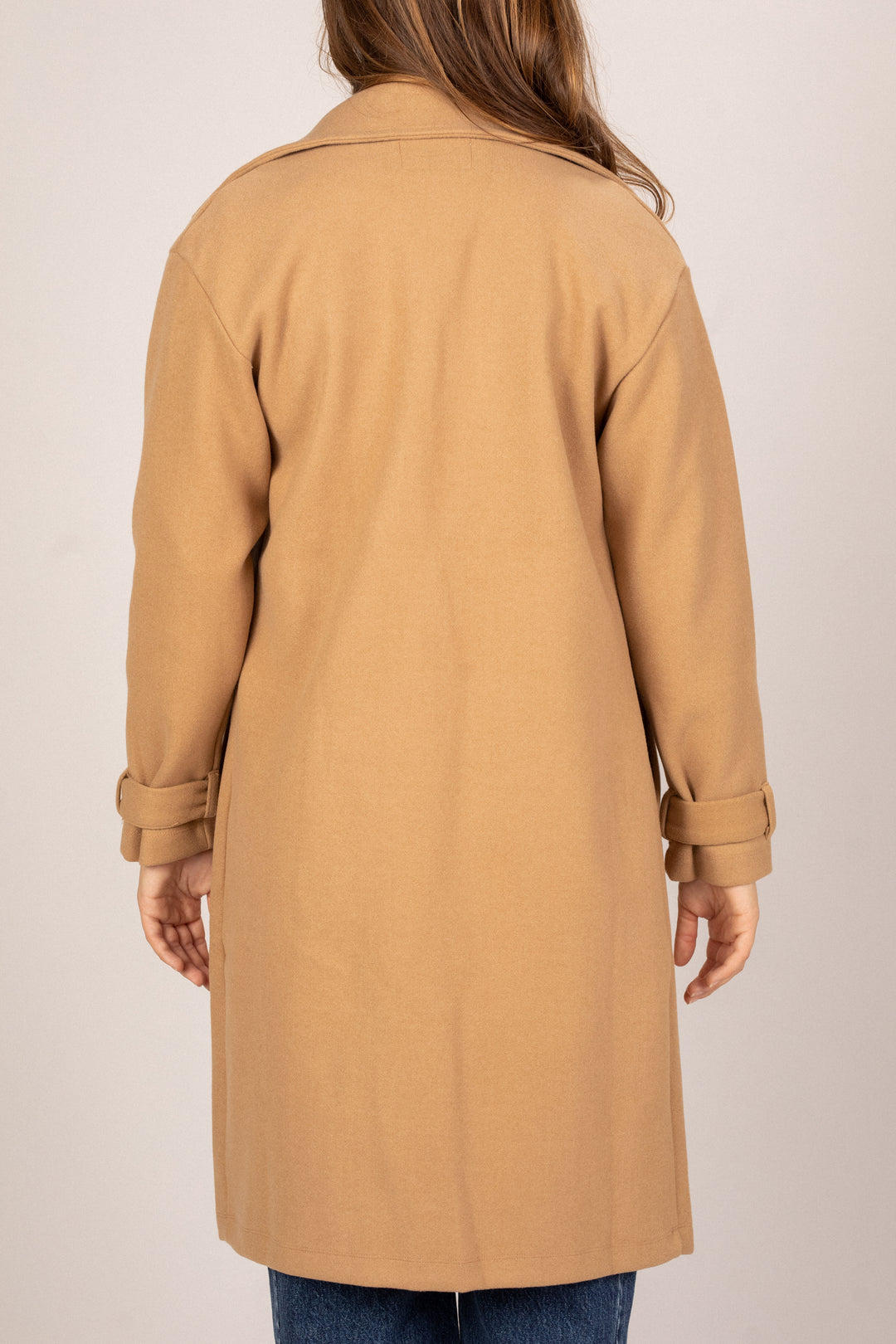 A tan colored trench coat with a notched collar and long sleeves, shown from the back on a model.