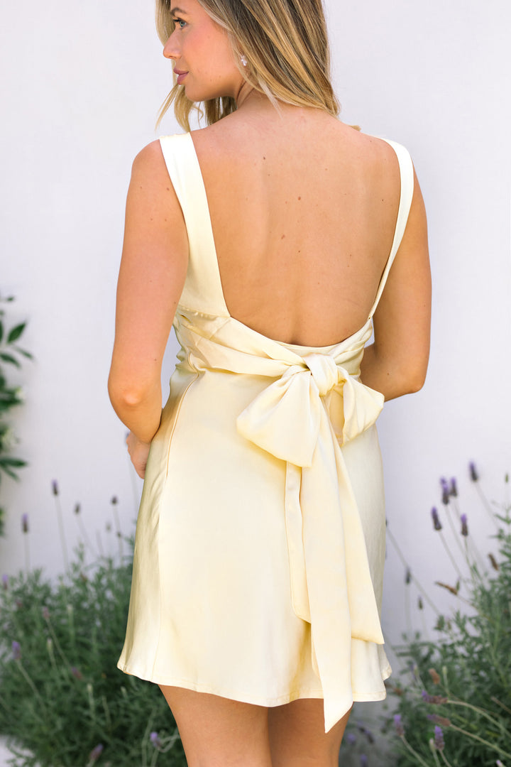 Backless yellow satin mini dress with a wraparound tie detail, creating a feminine, elevated look.