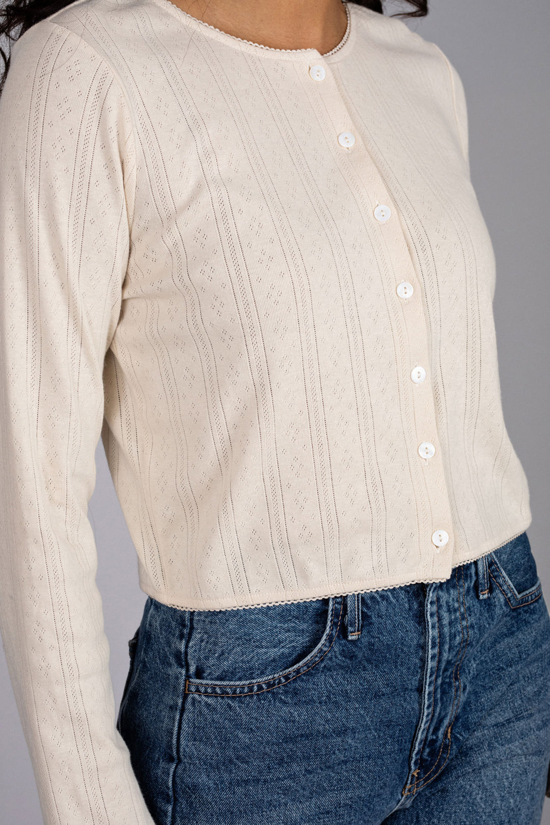 Cream-colored buttoned top with pointelle pattern details, worn with blue denim jeans.
