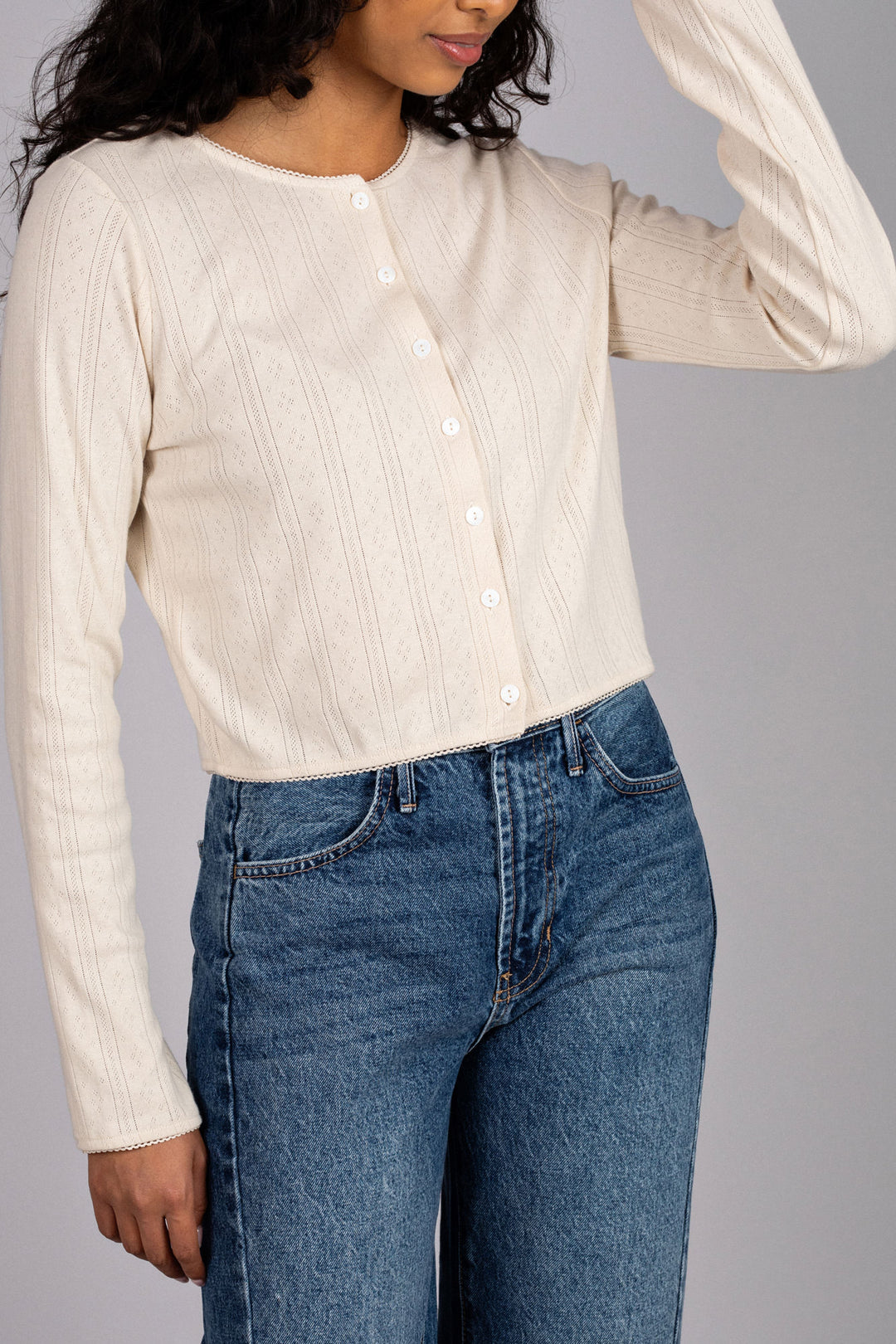 A beige buttoned top with a pointelle knit pattern, featuring long sleeves and a classic collar on a model wearing blue high-waisted jeans.