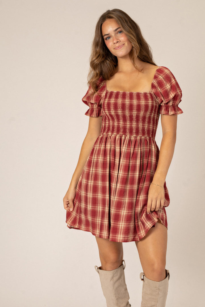 A plaid mini dress with puffed sleeves, a fitted bodice, and a flared, ruffled skirt in a deep red and beige plaid pattern.
