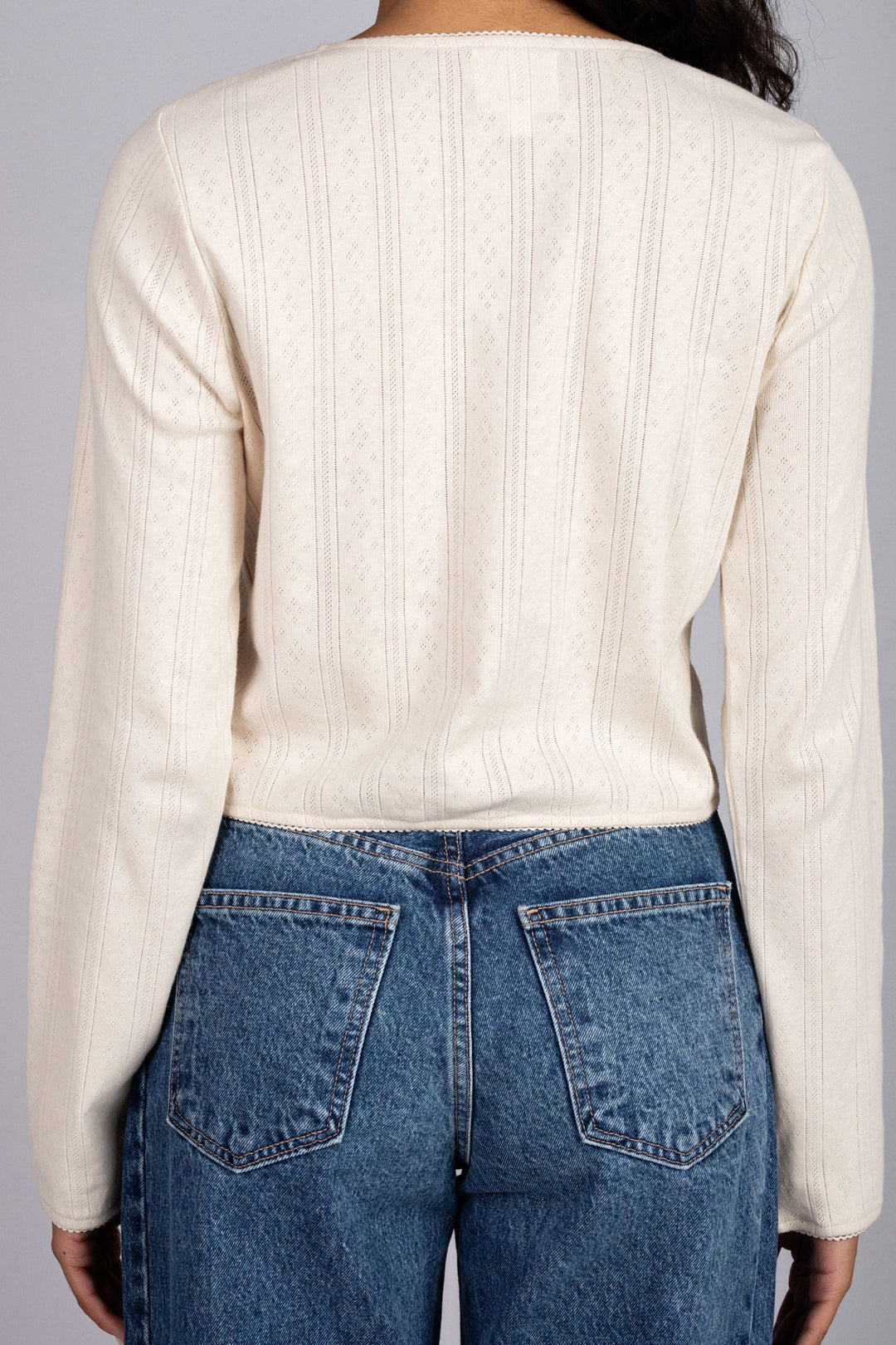 Cream-colored long-sleeved top with intricate pointelle knit patterns, worn with high-waisted denim jeans.