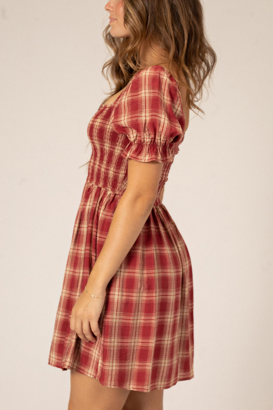 A red and tan plaid mini dress with a puff sleeve silhouette, elasticized waistband, and flared skirt.