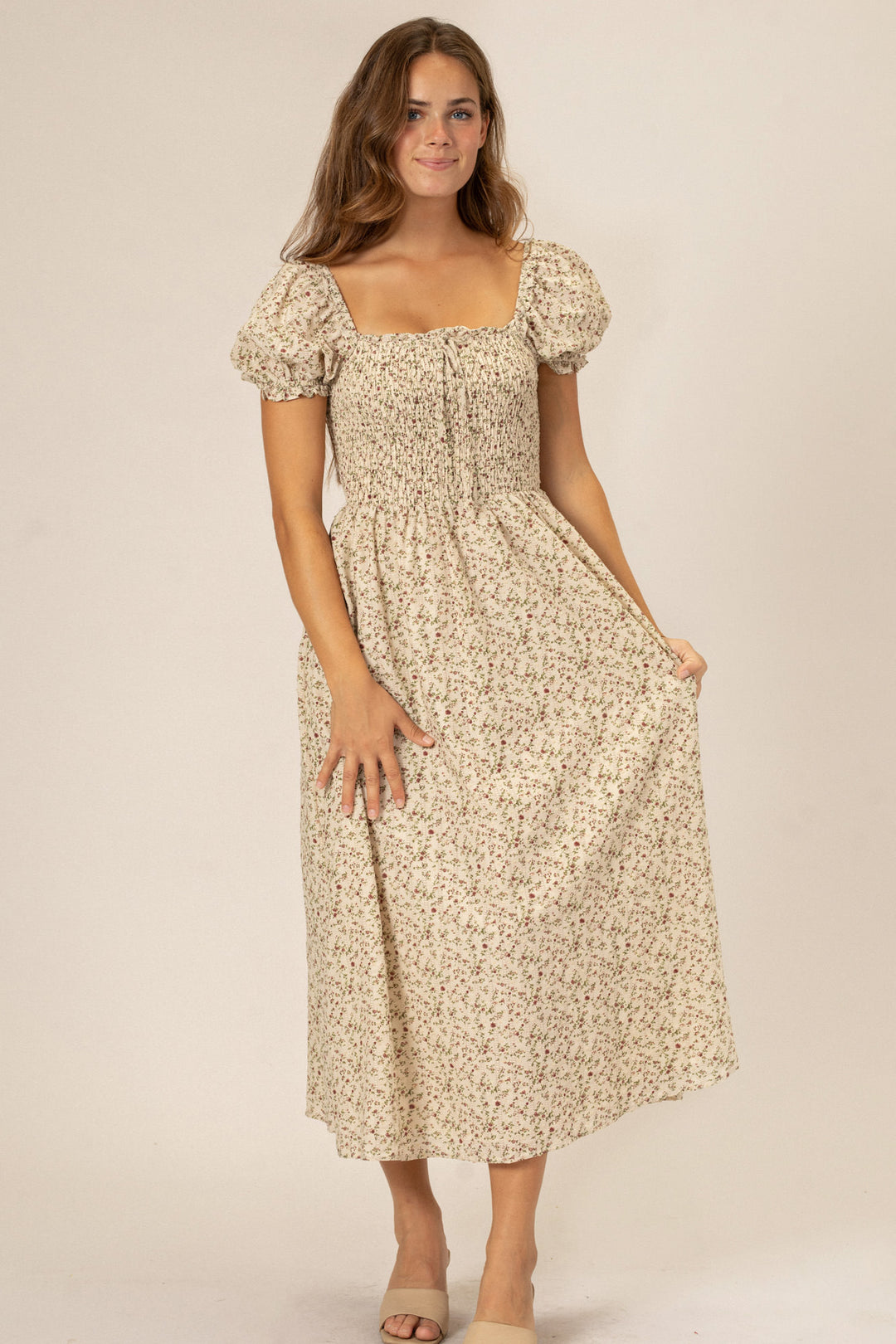 A beige floral print midi dress with puffed sleeves and a smocked bodice, featuring a flattering silhouette and fall-ready style.