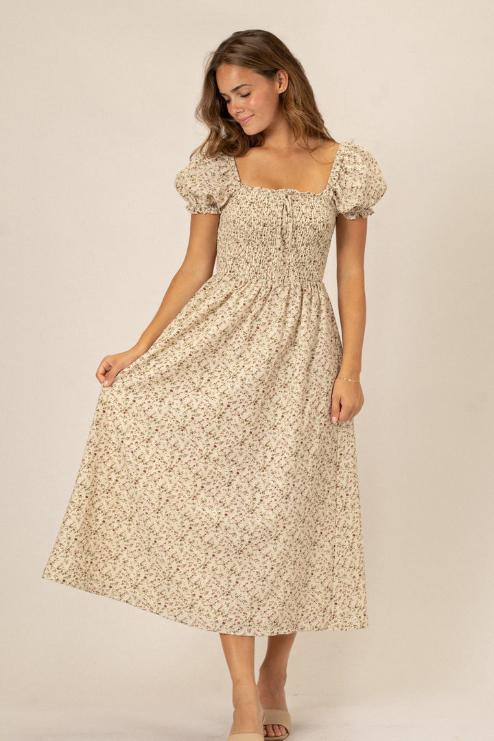 A flowing, beige midi dress with a floral print, puff sleeves, and a smocked waistline, showcasing a classic yet romantic style.